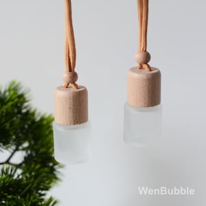 Può includere: Due bottiglie di vetro smerigliato con tappi di legno e cordini marroni. Le bottiglie sono appese ai cordini. Le bottiglie sono vuote e pronte per essere riempite con oli essenziali o altri liquidi.