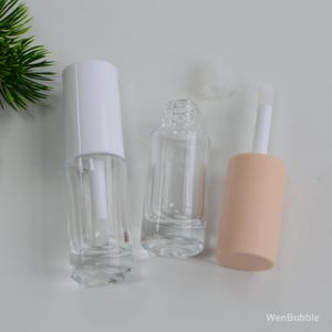 Peut inclure: Flacons de gloss transparents en verre avec des bouchons et applicateurs blancs. Un flacon a un bouchon blanc attach&eacute;, un autre est ouvert et le troisi&egrave;me a un bouchon couleur p&ecirc;che. Les flacons sont vides.