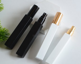 May include: Three glass perfume bottles with black, white, and gold caps. The bottles are square and have a minimalist design.