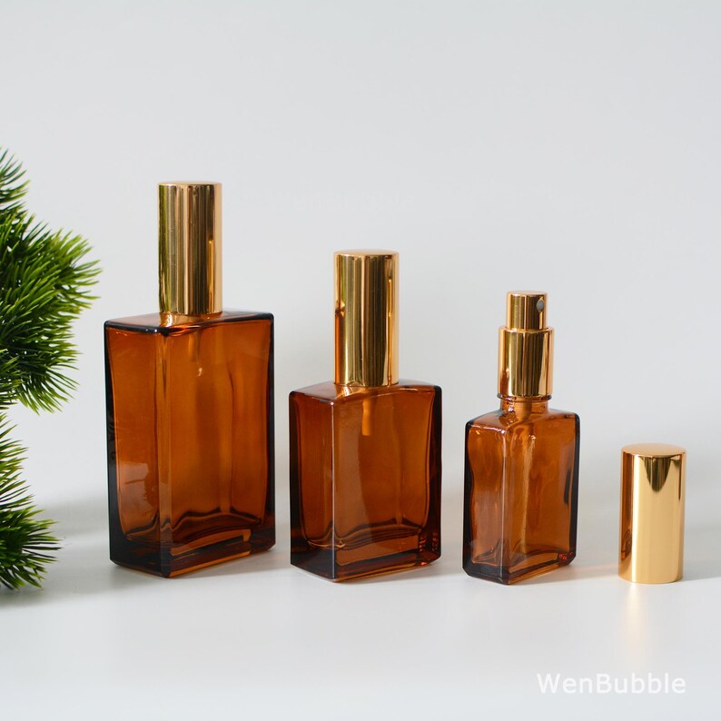 May include: Three amber glass bottles with gold spray tops and a gold cap. The bottles are different sizes and are arranged in a row from largest to smallest.