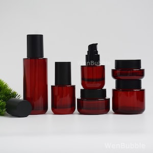 May include: A collection of dark red glass cosmetic containers with black lids, including two tall cylindrical bottles, one pump bottle, and two stacked jars. The text WenBubble is visible on the surface near the containers.