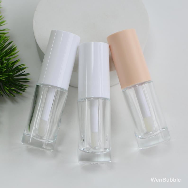 Peut inclure: Trois tubes de gloss transparents en verre avec des bouchons blancs et p&ecirc;che. Les tubes sont rectangulaires avec une baguette applicatrice transparente &agrave; l'int&eacute;rieur. Le fond est blanc avec une touche de vert.