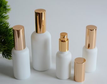 May include: Set of five white frosted glass bottles with gold colored caps. The bottles are various sizes and have a rounded shape.