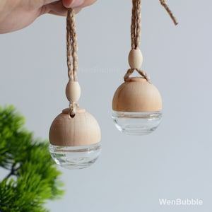 May include: Two wooden ball car air fresheners with glass vials hanging from twine cords with wooden beads. The cords are a natural beige colour with gold flecks.