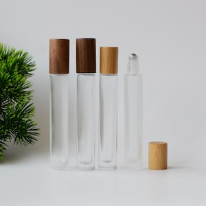 May include: Four clear glass roll-on bottles with wooden and bamboo caps. Three bottles have dark brown wooden caps, and one has a bamboo cap. One bottle has a silver rollerball. The bottles are arranged in a row.