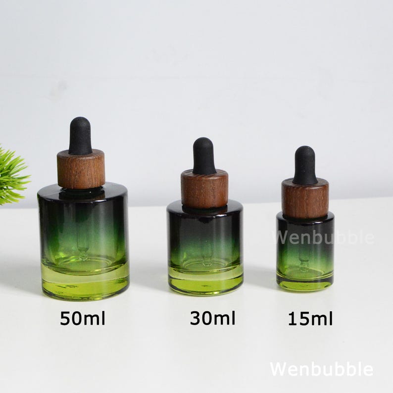 May include: Three glass dropper bottles in varying sizes: 50ml, 30ml, and 15ml. Each bottle has a dark green gradient, transitioning to clear at the base, with a wooden cap and black dropper. The bottles are labeled with their respective volumes.