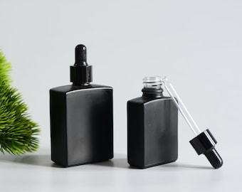 May include: Two black glass dropper bottles with black caps and droppers. The bottles are square shaped and have a frosted finish.