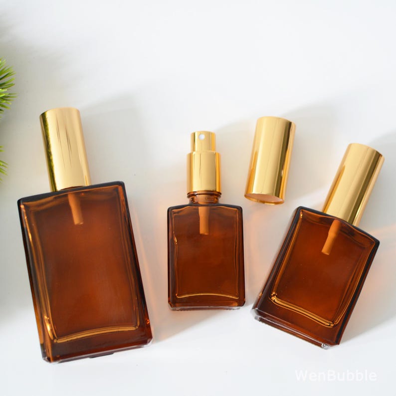 May include: Three amber glass bottles with gold spray tops. The bottles are of different sizes and are arranged in a row on a white surface.