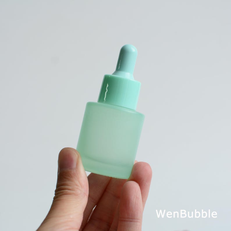 May include: A frosted glass dropper bottle in a soft mint green color. The bottle has a matching mint green dropper top. The bottle is held in a hand against a white background. The text "WenBubble" is in the bottom right corner.