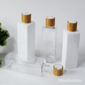 May include: Four clear square bottles with white lids and bamboo caps. The bottles are empty and ready to be filled with your favorite liquids.
