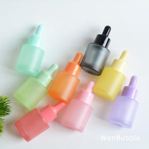May include: An assortment of colorful frosted glass dropper bottles in various shades, including green, orange, pink, yellow, and purple. The bottles have matching colored droppers and a frosted finish. The text "WenBubble" is visible in the bottom right corner.