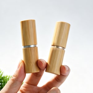 May include: Two cylindrical containers made of light brown bamboo with a visible wood grain texture. Each container features a horizontal silver-colored metal band separating the top cap from the base, creating a sleek and uniform appearance.
