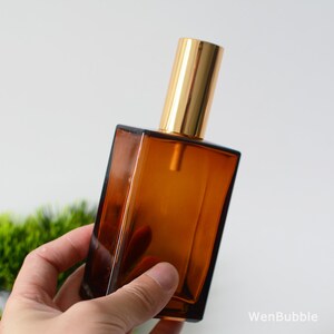May include: A brown glass bottle with a gold spray nozzle. The bottle is rectangular and has a square base.