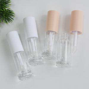 Peut inclure: Tubes de brillant &agrave; l&egrave;vres transparents et vides, avec des bouchons blancs et p&ecirc;che. Les tubes transparents montrent les baguettes applicatrices &agrave; l'int&eacute;rieur. Un bouchon est retir&eacute;, r&eacute;v&eacute;lant la baguette. Sur fond blanc.