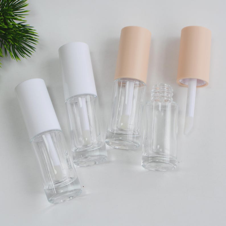 Peut inclure: Tubes de brillant &agrave; l&egrave;vres transparents et vides, avec des bouchons blancs et p&ecirc;che. Les tubes transparents montrent les baguettes applicatrices &agrave; l'int&eacute;rieur. Un bouchon est retir&eacute;, r&eacute;v&eacute;lant la baguette. Sur fond blanc.