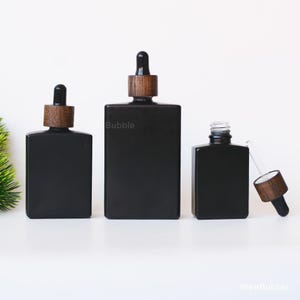 Peut inclure: Trois flacons compte-gouttes en verre noir avec des bouchons en bois. Les flacons sont rectangulaires et de tailles différentes. Un flacon a un dessus ouvert avec une pipette en verre. Le mot "Bubble" est imprimé sur le flacon du milieu.