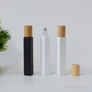 May include: Three glass roller bottles with bamboo caps. The bottles are square shaped and come in black and white. The bottles are empty and ready to be filled with essential oils or other liquids.