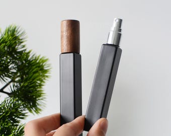 May include: Two black glass perfume bottles with different tops. One bottle has a wooden top and the other has a silver spray top.