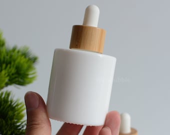 May include: White glass bottle with a bamboo dropper lid. The bottle is opaque and has a smooth, rounded shape.