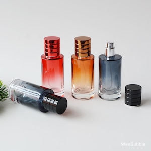 May include: Four glass perfume bottles with metallic caps. One bottle is lying on its side. The bottles are red, orange, and blue, with matching colored caps. The caps are a shiny metallic finish. The bottles are empty.