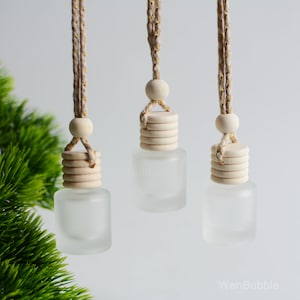 Puede incluir: Tres botellas de vidrio esmerilado con tapones de madera y colgadores de cuerda. Las botellas están vacías y listas para ser llenadas con aceites esenciales o fragancia.