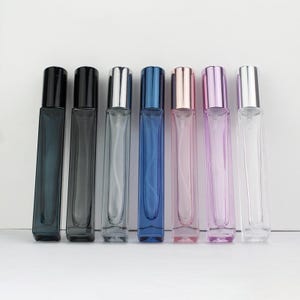 Puede incluir: Siete botellas de vidrio transparente con tapas de diferentes colores. Las botellas son todas del mismo tamaño y forma, y están dispuestas en una fila de izquierda a derecha. Las tapas son negras, plateadas, azules, rosas y transparentes.