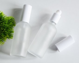 May include: Two frosted glass bottles with white spray tops and a white cap. The bottles are on a white surface.