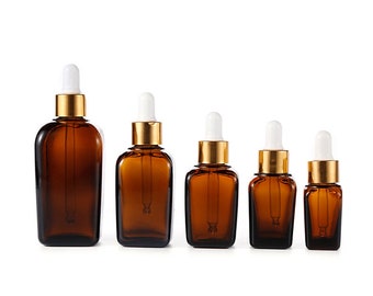 May include: Set of five amber glass dropper bottles with gold caps and white droppers. The bottles are arranged in order of size, with the largest bottle on the left and the smallest bottle on the right.