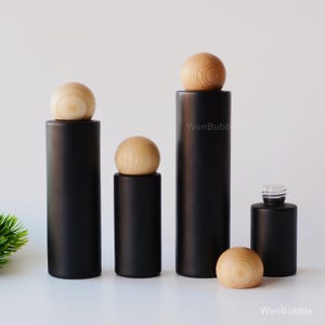 Pode incluir: Uma coleção de garrafas cilíndricas pretas com rolhas esféricas de madeira. As garrafas variam em altura e estão dispostas sobre um fundo branco. O texto "WenBubb" é visível.