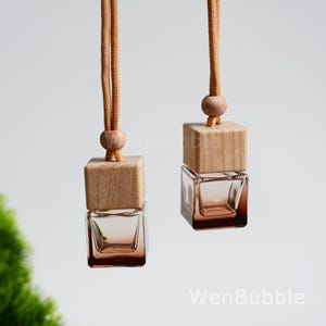 Peut inclure: Deux désodorisants de voiture suspendus. Chacun a une petite bouteille carrée en verre avec un dessus en bois et un cordon marron. Le verre est teinté d'une couleur marron clair. Le dessus en bois est de couleur marron clair.