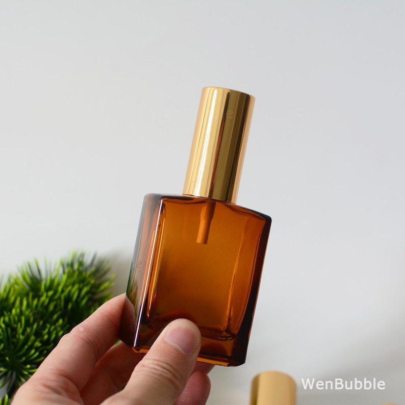 May include: A brown glass bottle with a gold spray top. The bottle is square shaped and has a frosted finish.
