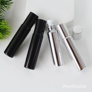 May include: An assortment of roll-on perfume bottles. Two are black, and two are silver. One silver bottle has a white rollerball. The bottles are cylindrical with matching caps. The background is white.