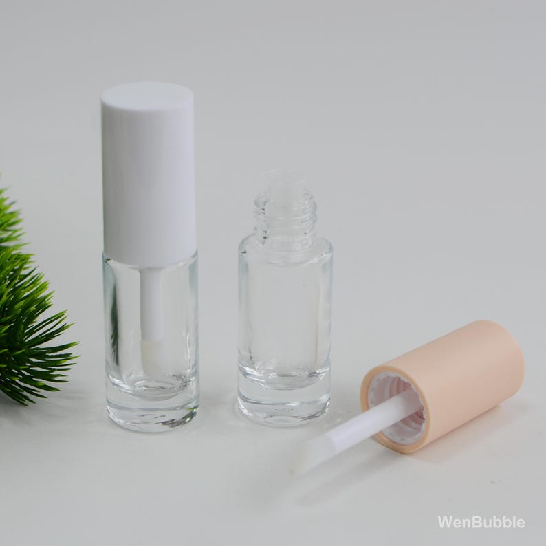 Peut inclure: Flacons de gloss transparents avec des bouchons blancs et p&ecirc;che. Un flacon est ouvert, r&eacute;v&eacute;lant la baguette applicatrice. Les flacons sont vides et pr&ecirc;ts &agrave; &ecirc;tre remplis de gloss ou d'autres produits cosm&eacute;tiques.