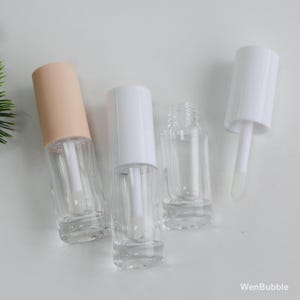 Peut inclure: Tubes de brillant &agrave; l&egrave;vres transparents avec des bouchons blancs et p&ecirc;che. Les tubes sont vides, avec des applicateurs visibles &agrave; l'int&eacute;rieur. L'image est prise sur une surface blanche.