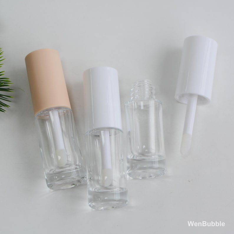 Peut inclure: Tubes de brillant &agrave; l&egrave;vres transparents avec des bouchons blancs et p&ecirc;che. Les tubes sont vides, avec des applicateurs visibles &agrave; l'int&eacute;rieur. L'image est prise sur une surface blanche.