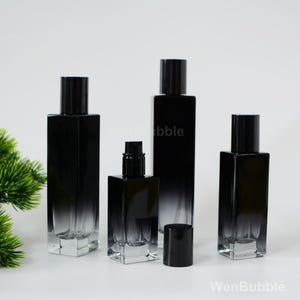 May include: Four black glass perfume bottles with a gradient effect. The bottles have black caps and are arranged in a row on a white surface.