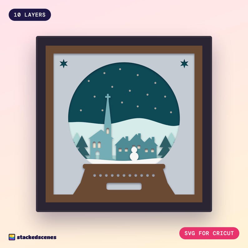 Finished 10-layer Snow Globe Village paper shadow box: a church spire, cottages with glowing windows and a snowman inside a snow globe on a wooden base.