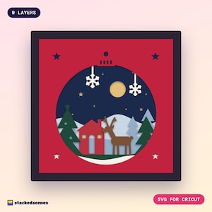 Finished 9-layer Christmas bauble paper shadow box: a snowy woodland with a red cabin, reindeer and pines seen through a red bauble-shaped window.