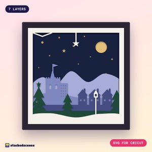 Finished 7-layer Winter Glen paper shadow box in a dark frame: a castle, village, pines and a hanging star under a gold moon on a navy night sky.