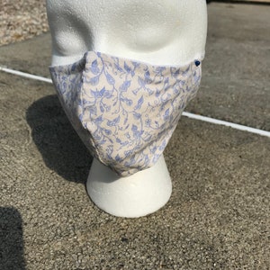 Op de afbeelding: Een wit gezichtmasker met een blauw en wit bloemenpatroon. Het masker zit op een wit mannequinhoofd.
