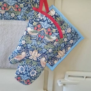 May include: A blue oven glove and pot holder set with a floral and bird design. The set has a red trim and is hanging on a metal hook. The pattern includes birds, flowers, and berries.