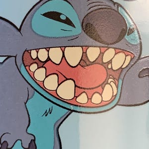 May include: A blue and gray cartoon character with a wide open mouth and large teeth. The character has a blue eye and a black nose. The character is on a light blue background.