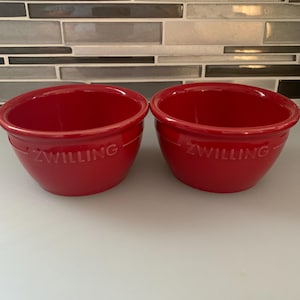 Op de afbeelding: Twee rode keramische kommen met het woord "Zwilling" erop gegraveerd.