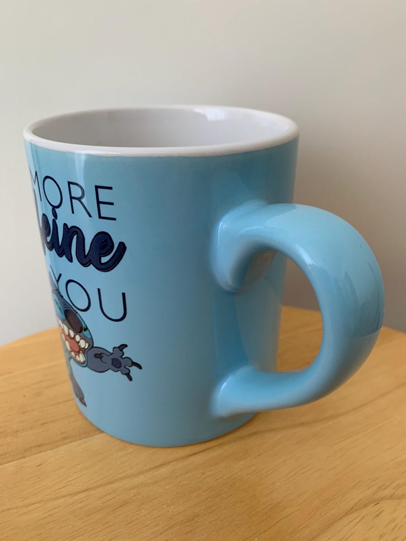 May include: A light blue ceramic mug with a cartoon character on it. The mug has the text "More Caffeine You" on it.