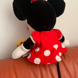 Może przedstawiać: Pluszowa zabawka Minnie Mouse z czarnymi uszami, czerwoną sukienką w białe kropki i czarnym ogonem.