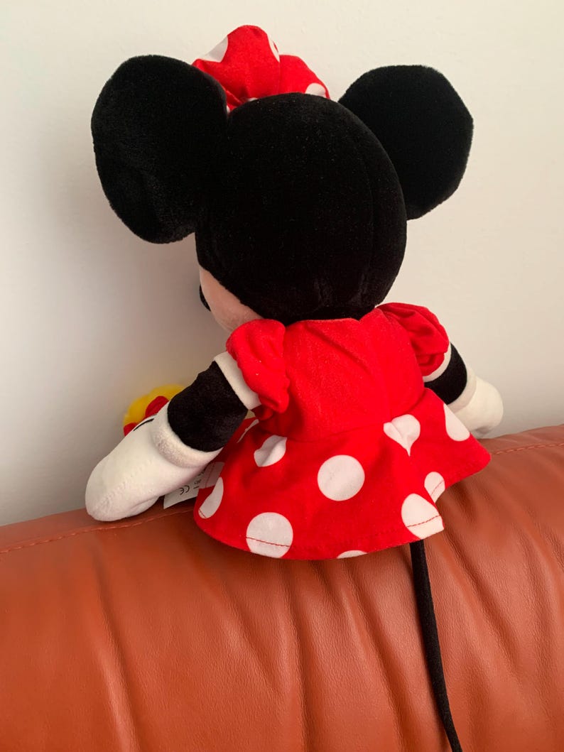 Może przedstawiać: Pluszowa zabawka Minnie Mouse z czarnymi uszami, czerwoną sukienką w białe kropki i czarnym ogonem.
