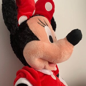 May include: A plush red and black Minnie Mouse toy with white polka dots. The toy is wearing a red bow with white polka dots and a red dress with white polka dots.