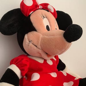 Może przedstawiać: Pluszowa zabawka przedstawiająca Minnie Mouse w czerwonej sukience w białe kropki i z czerwoną kokardką w białe kropki.