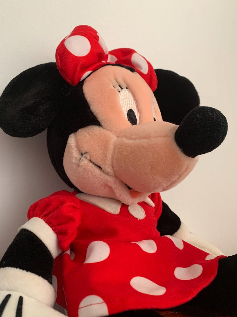 Może przedstawiać: Pluszowa zabawka przedstawiająca Minnie Mouse w czerwonej sukience w białe kropki i z czerwoną kokardką w białe kropki.