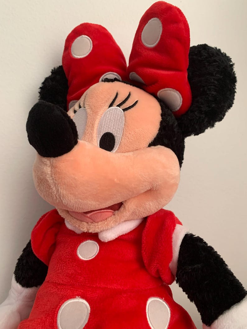 May include: A plush red and black Minnie Mouse toy with a white polka dot bow and dress. The toy has a friendly expression and is made of soft, cuddly material.